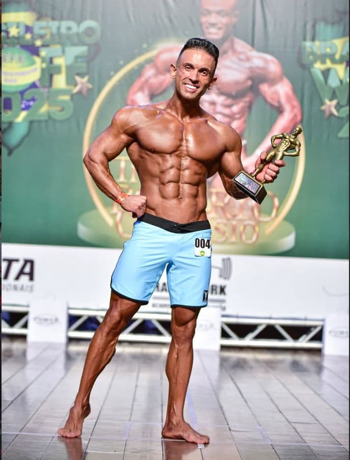 Bruno Rosa no palco de competição, campeão mundial de fisiculturismo, segurando troféu